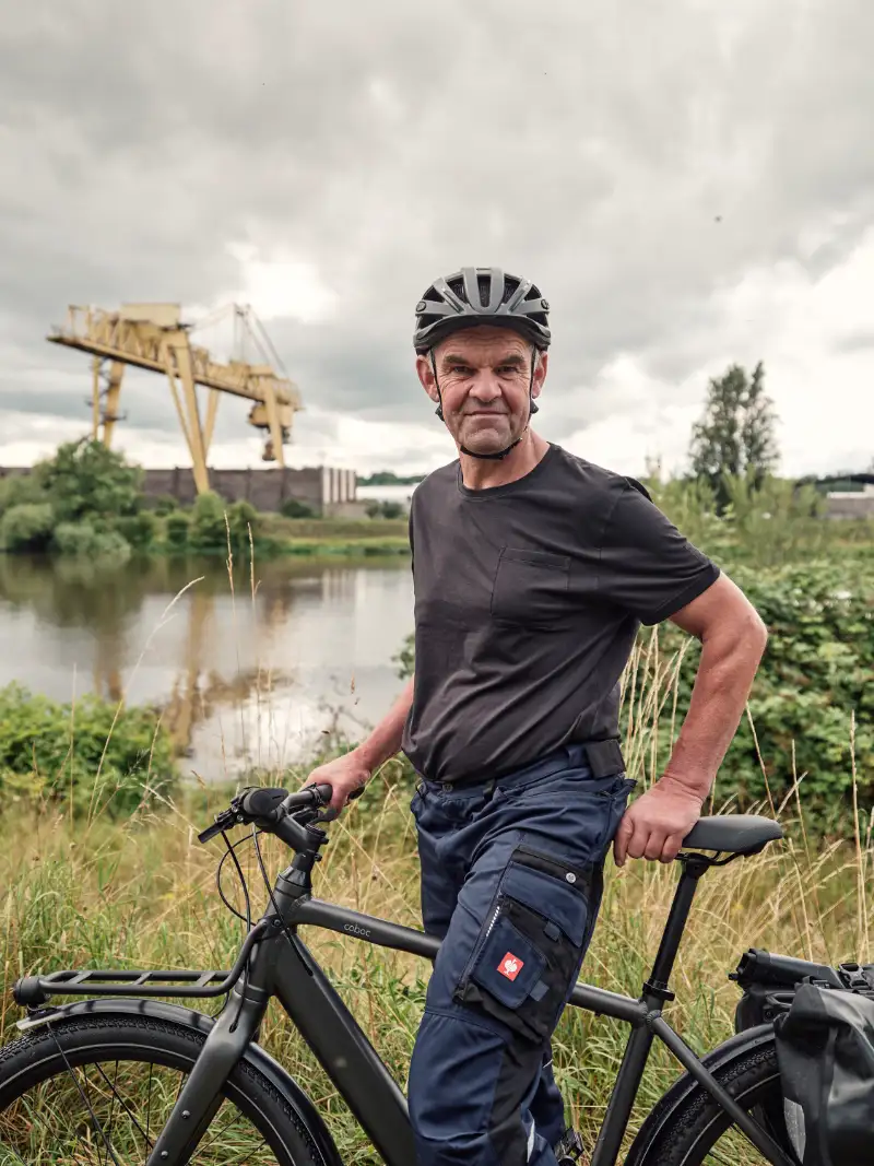 JobRadler in Arbeitskleidung im Grünen mit Kran im Hintergrund