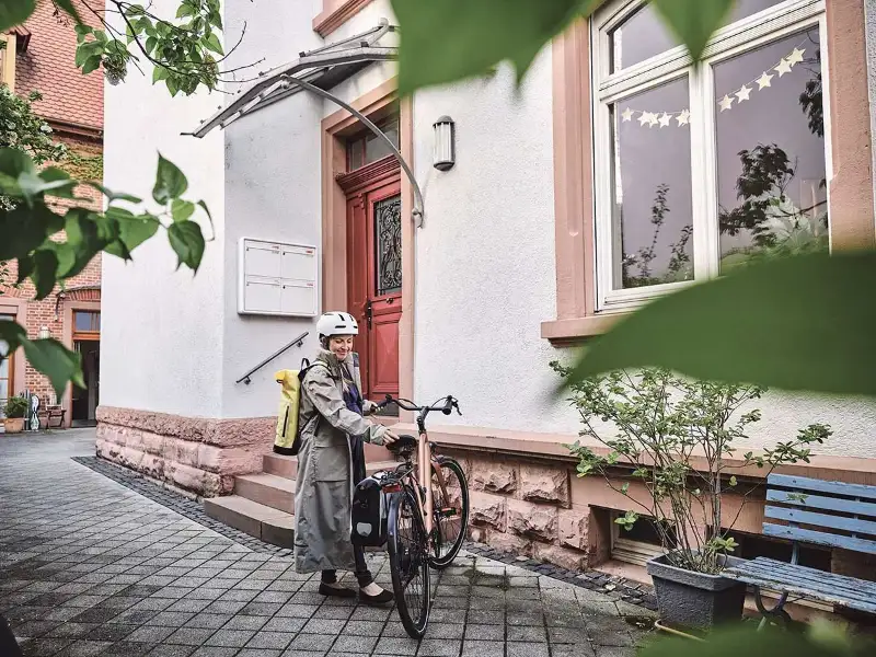Eine selbstständige Pendlerin mit Regenmantel steht in urbaner Gegend neben ihrem Fahrrad Eine selbstständige Pendlerin mit Regenmantel steht in urbaner Gegend neben ihrem Fahrrad