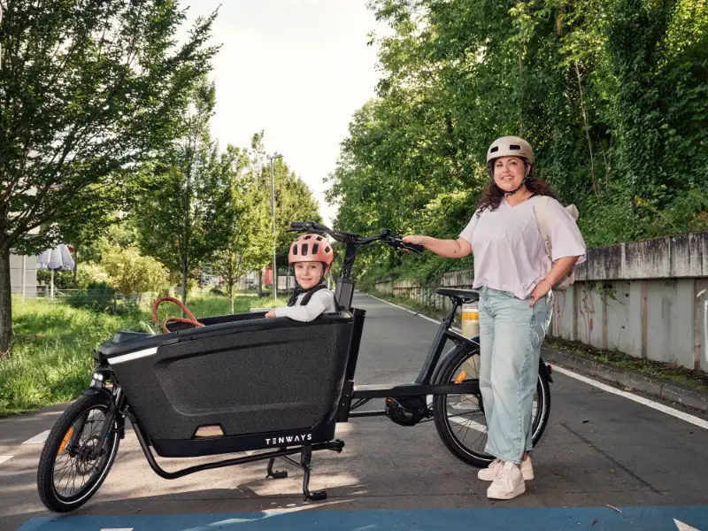 JobRadlerin posiert stolz neben ihrem Lastenrad mit Kind auf der Fahrradstraße JobRadlerin posiert stolz neben ihrem Lastenrad mit Kind auf der Fahrradstraße