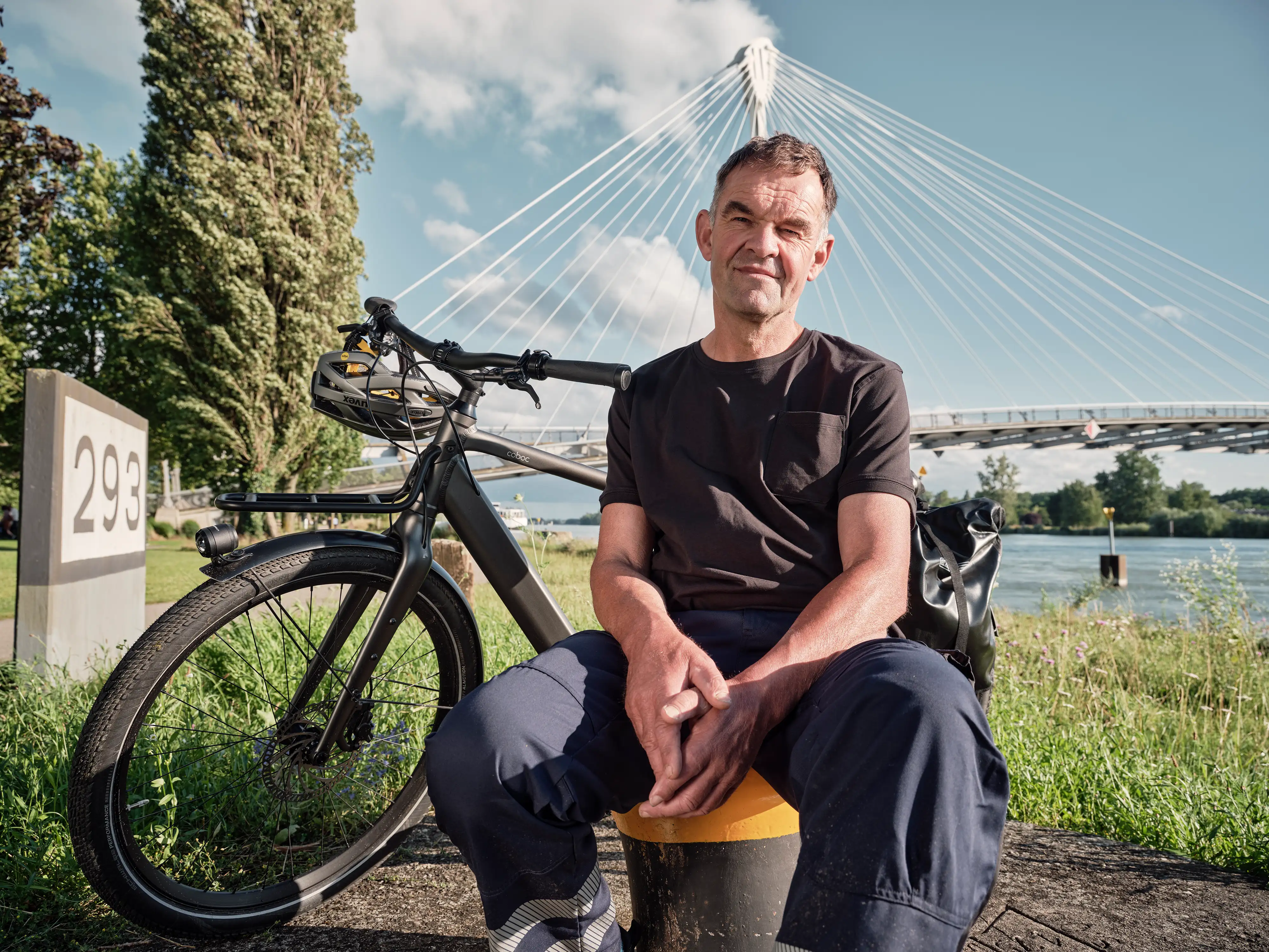 Ein Mann sitzt vor einer Brücke auf einem Poller. Hinter ihm steht sein Fahrrad. Ein Mann sitzt vor einer Brücke auf einem Poller. Hinter ihm steht sein Fahrrad.