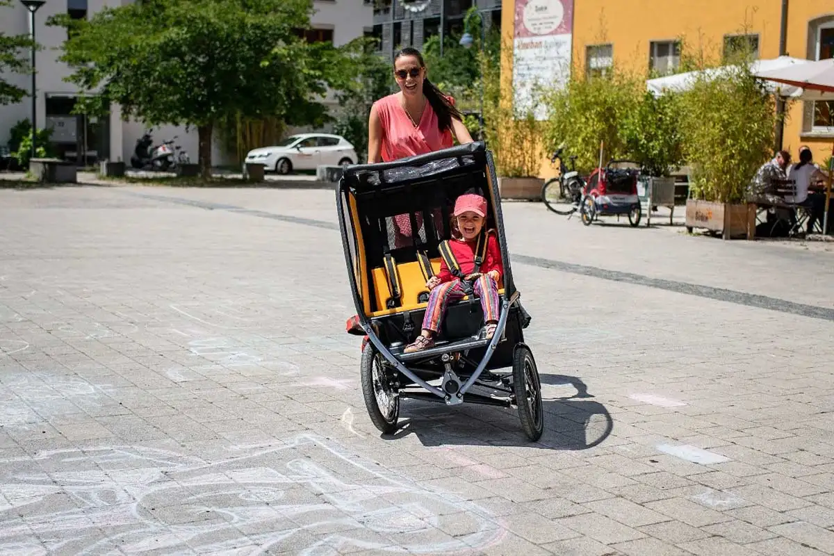 Eine Mutter fährt das Chike e-Bike in der Stadt. Ihr Kind sitzt angeschnallt darin. Beide lachen